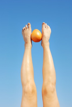 стройные женские ноги сжимают ступнями апельсин