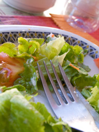 недоеденный салат из помидор огурцов и латука в тарелке с вилкой