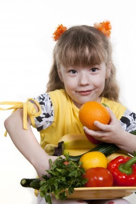 полненькая девочка перед миской с фруктами и овощами